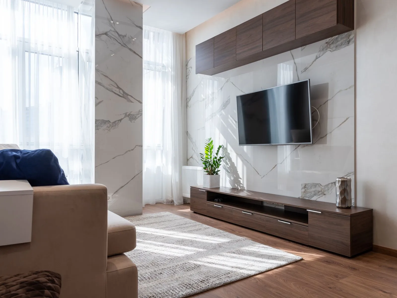A bright, modern condo living room with wood floors, a marble accent wall, and a comfortable sofa